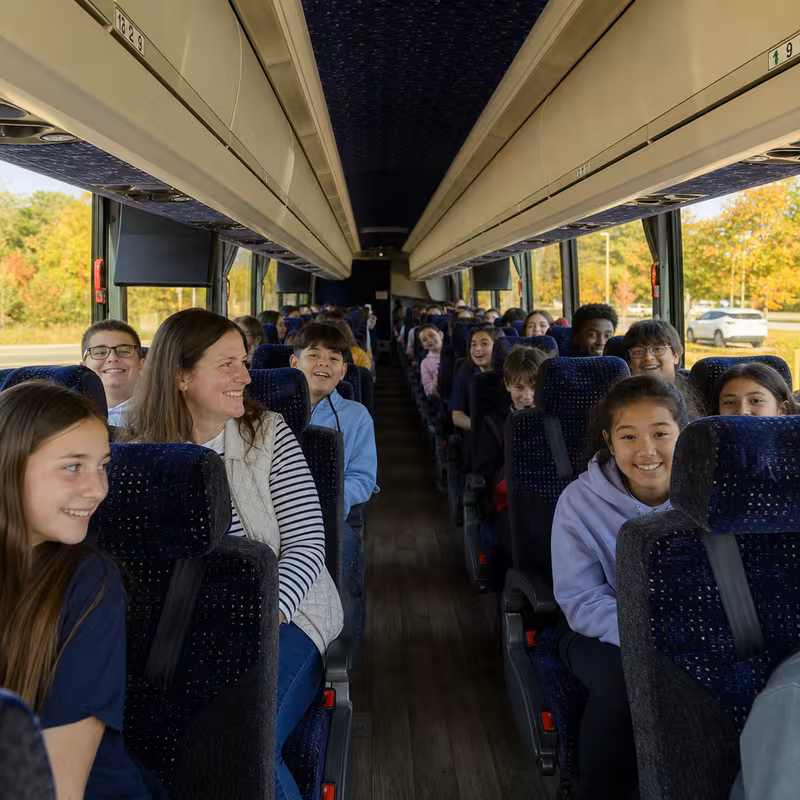 Group boarding a white charter bus for School Transportation transportation in Aurora